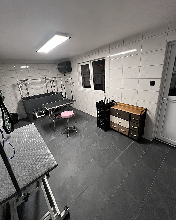 Binnen in de salon: witte tegels, donkere vloer, trimtafels en een hondenbad