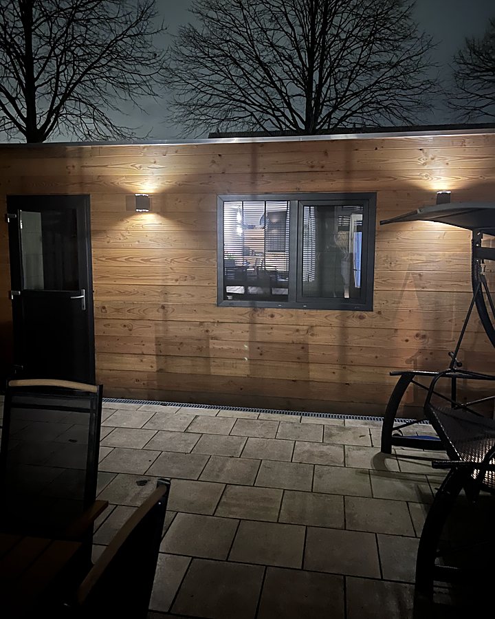 De salon in de tuin, een houten gebouwtje met lampen aan de gevel, 's avonds